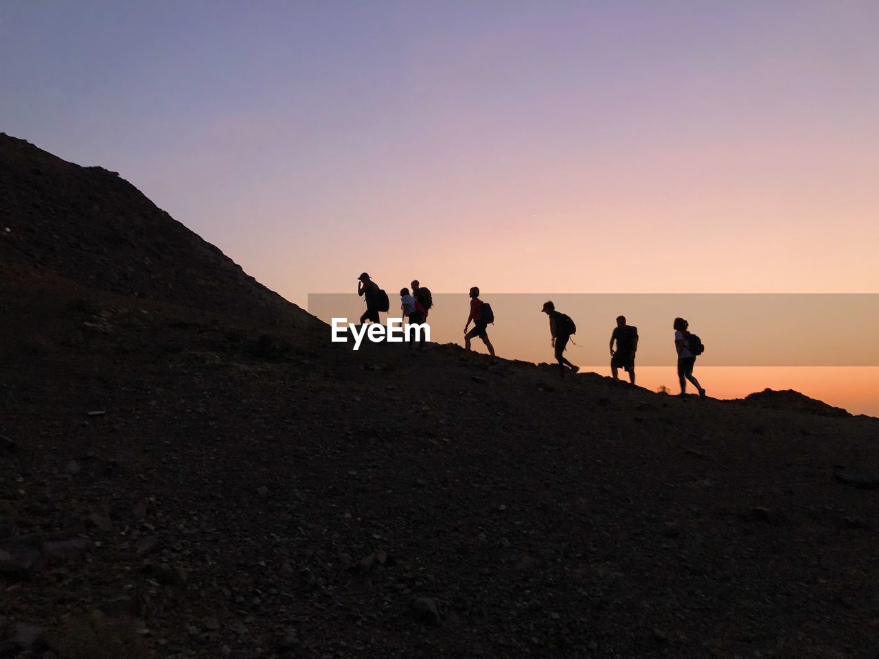 Group of people on the mountain during evening walk against sky during sunset