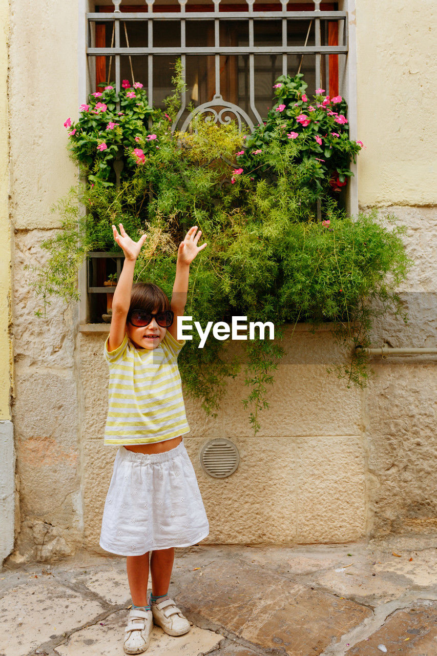 Small happy girl in big sunglasses posing next to old building outdoors
