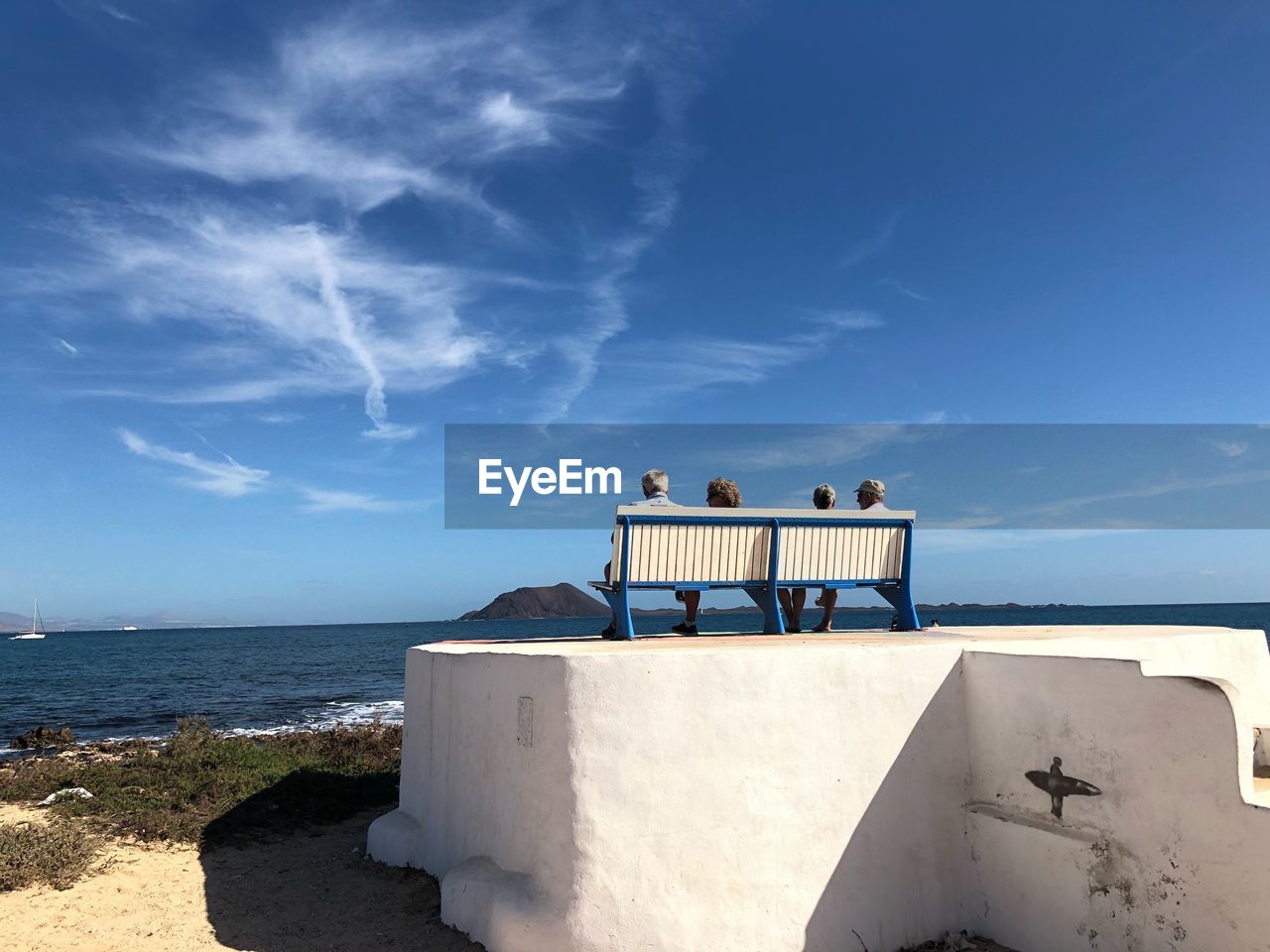 Rear view of people sitting on beach against sky