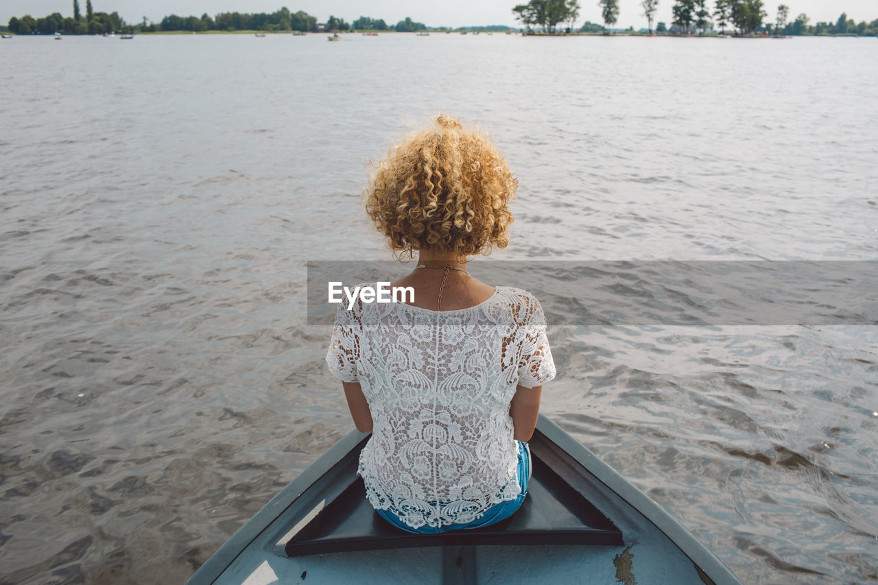 Rear view of mid adult woman sitting in boat on lake