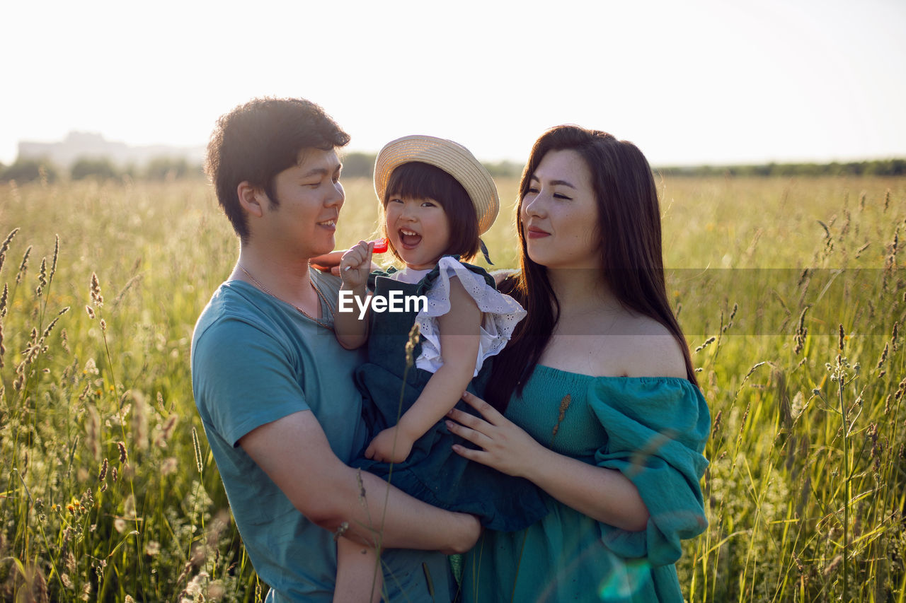 Korean family mom and father with a girl child daughter with candy lying on a green field in summer