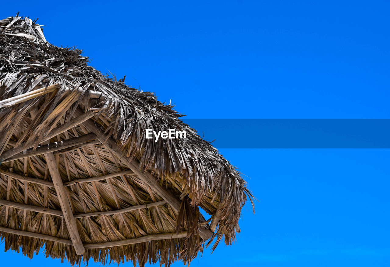Low angle view of thatched roof against clear blue sky