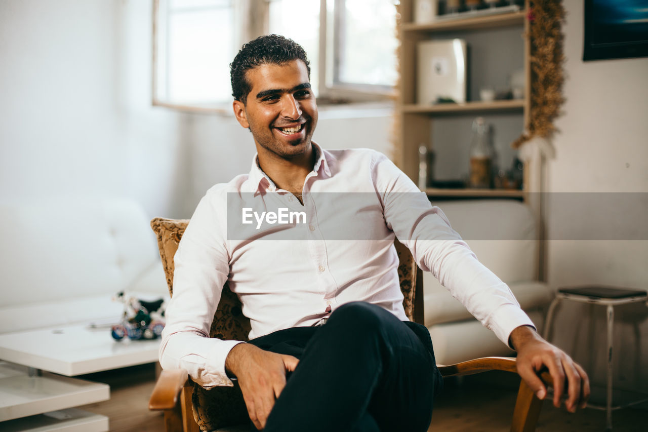 Smiling young man sitting on chair at home