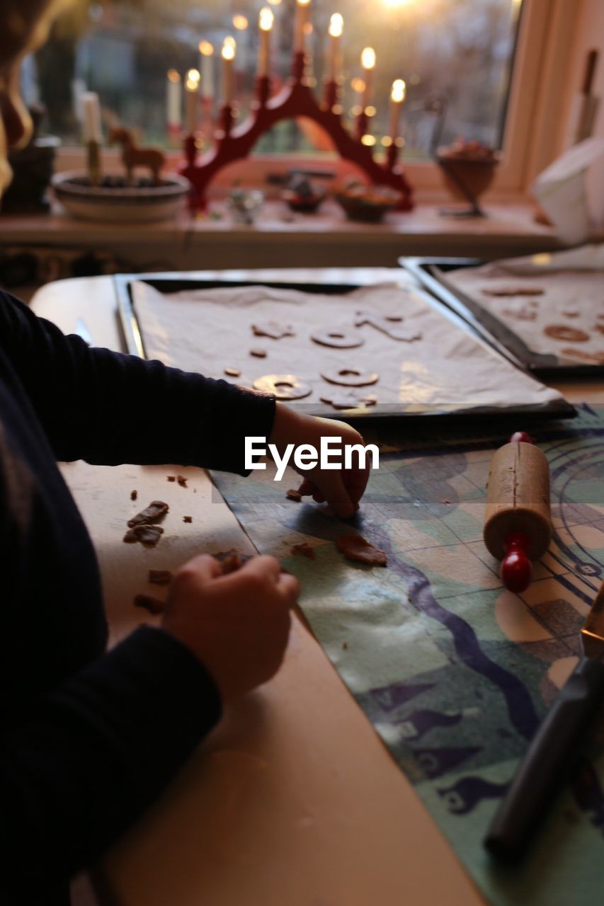 Midsection of girl preparing gingerbread cookies at table in kitchen