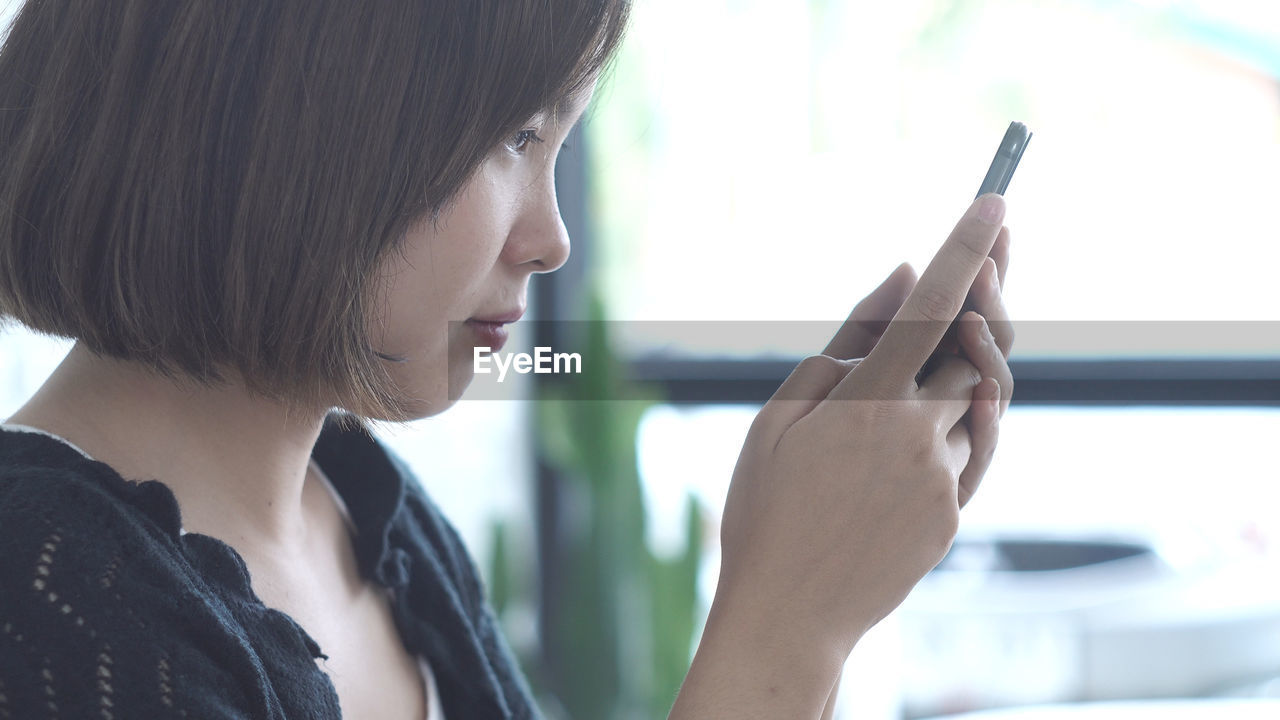 Close-up of woman using phone while standing against wall