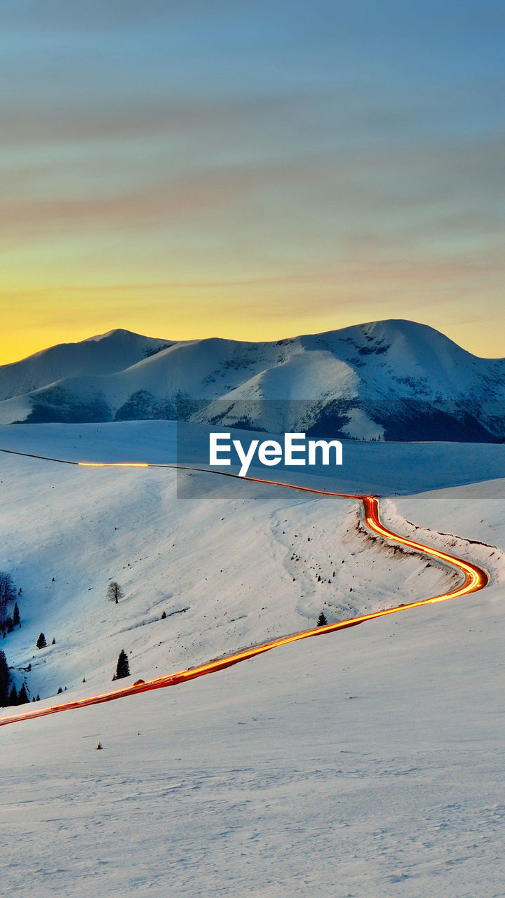 Scenic view of mountains against cloudy sky during winter at sunset