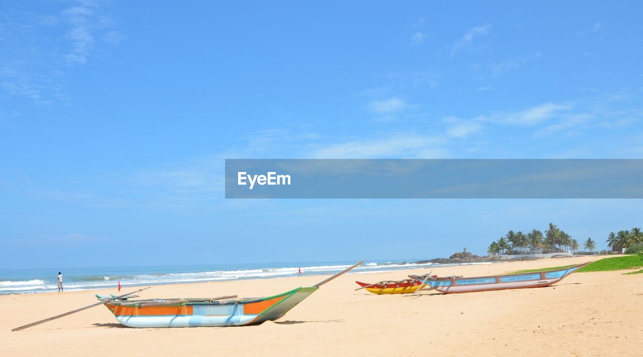 BOATS MOORED ON BEACH AGAINST SKY