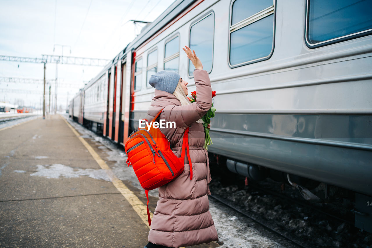 Girl with a red backpack and flowers waves to a departing train