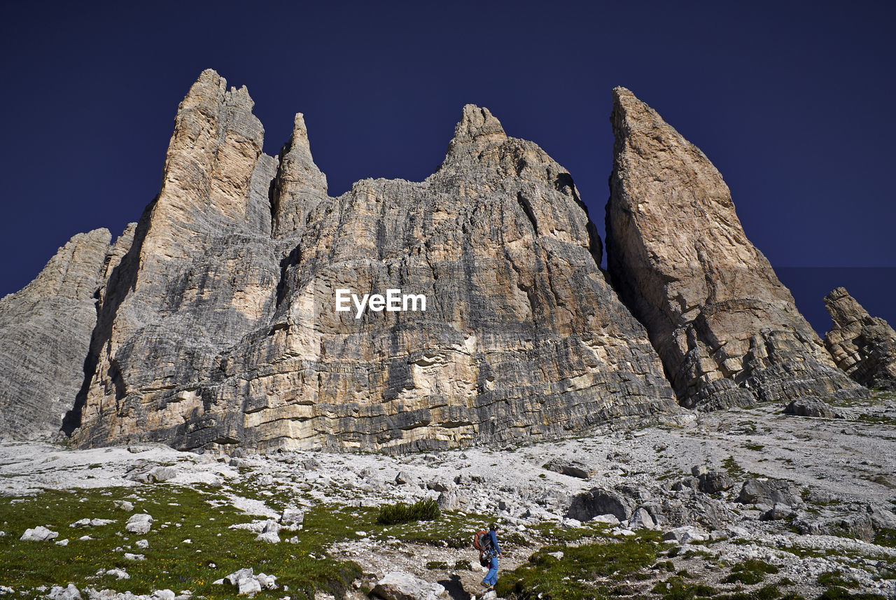 Low angle view of man climbing towards rocky mountains against sky