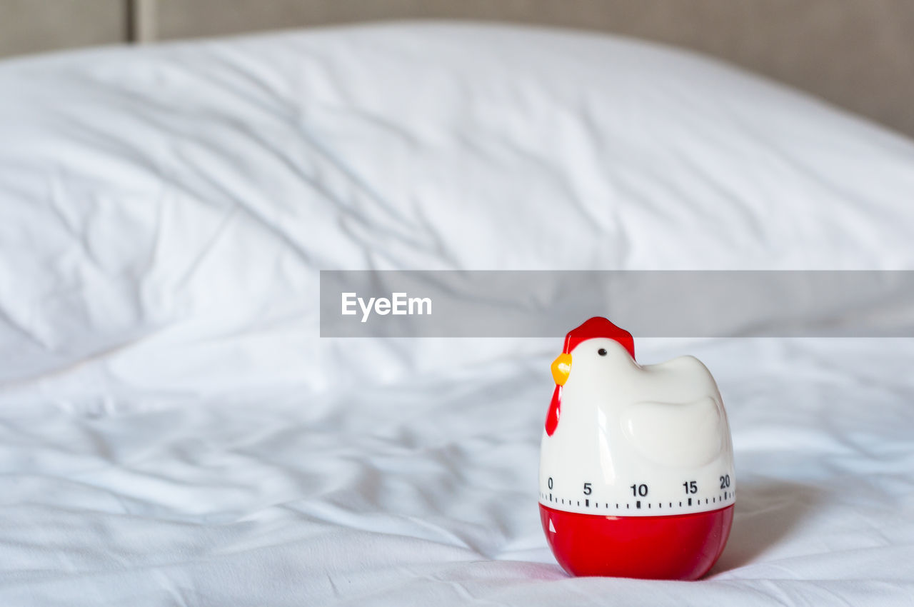Modern chicken timer on white bed white pillow in bedroom, bell timer lay on resting place.