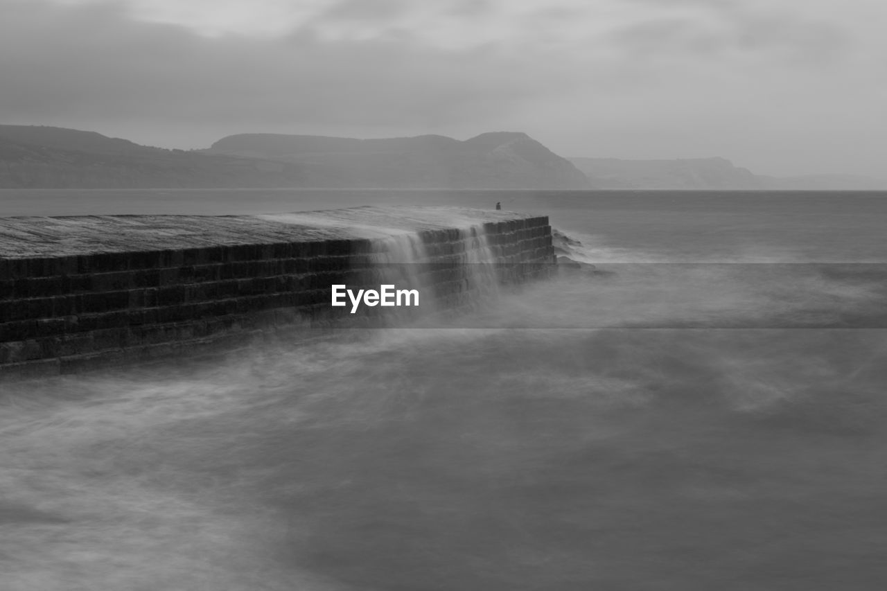 Long exposure of the waves crashing up against the pier at lyme regis in dorset in black and white