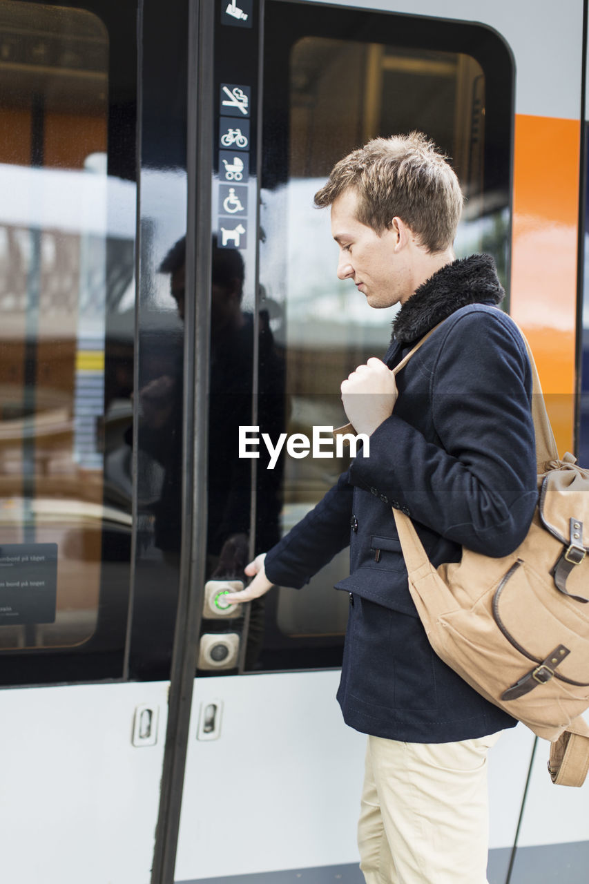 Side view of young businessman pressing door button while boarding train