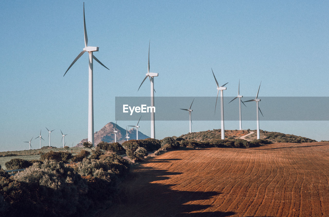 Windmills on landscape against clear blue sky