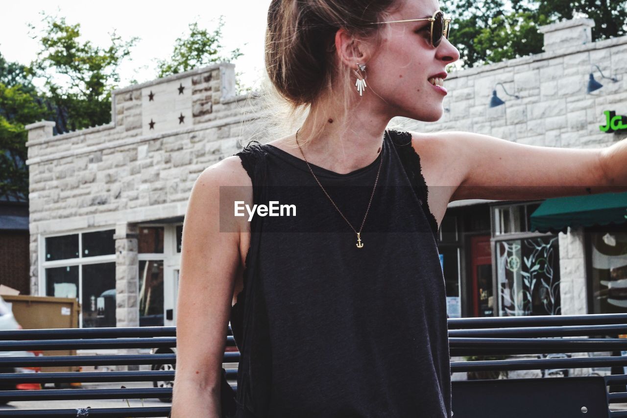 Young woman wearing sunglasses while standing against building