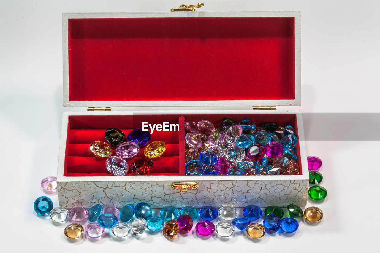 Close-up of colorful gemstones and box over white background