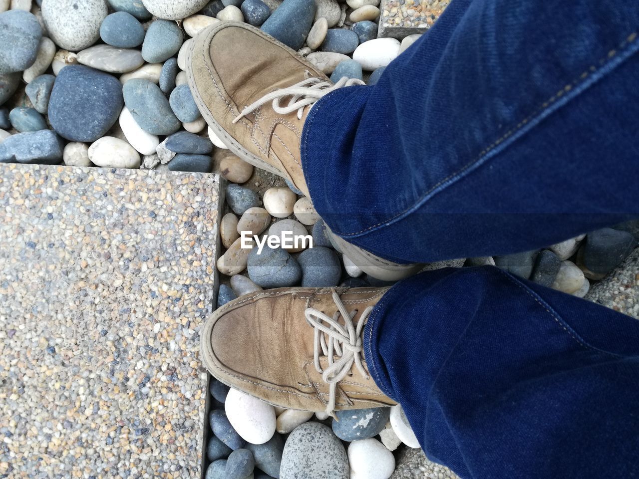 Low section of man standing on pebbles