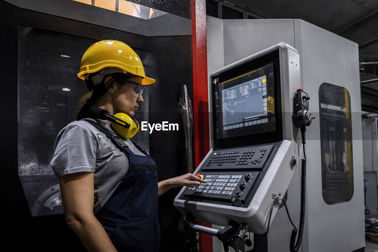 Engineer wearing hardhat operating cnc machine keypad in modern factory