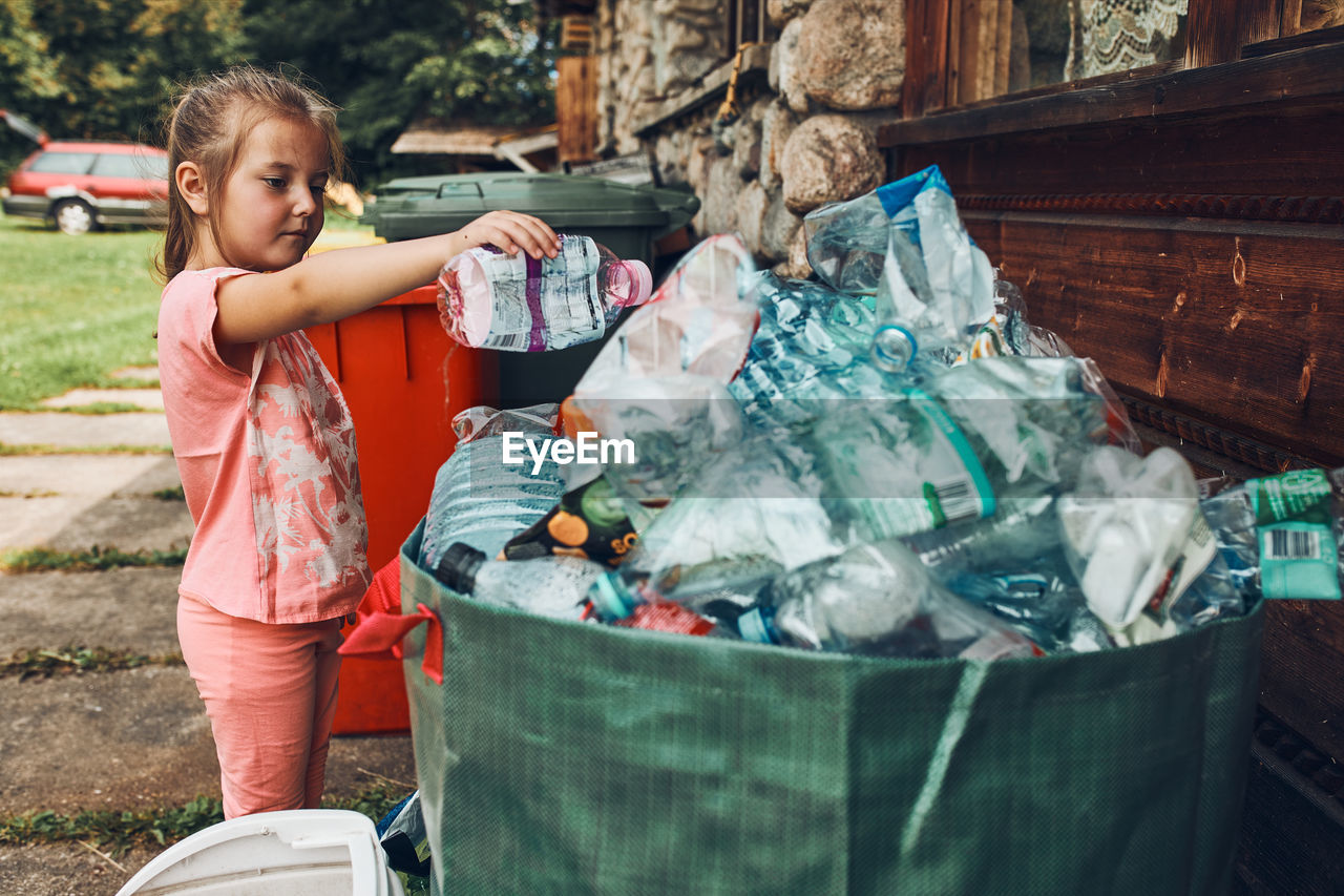 Child little girl throwing out plastic bottle to big container full of plastic waste