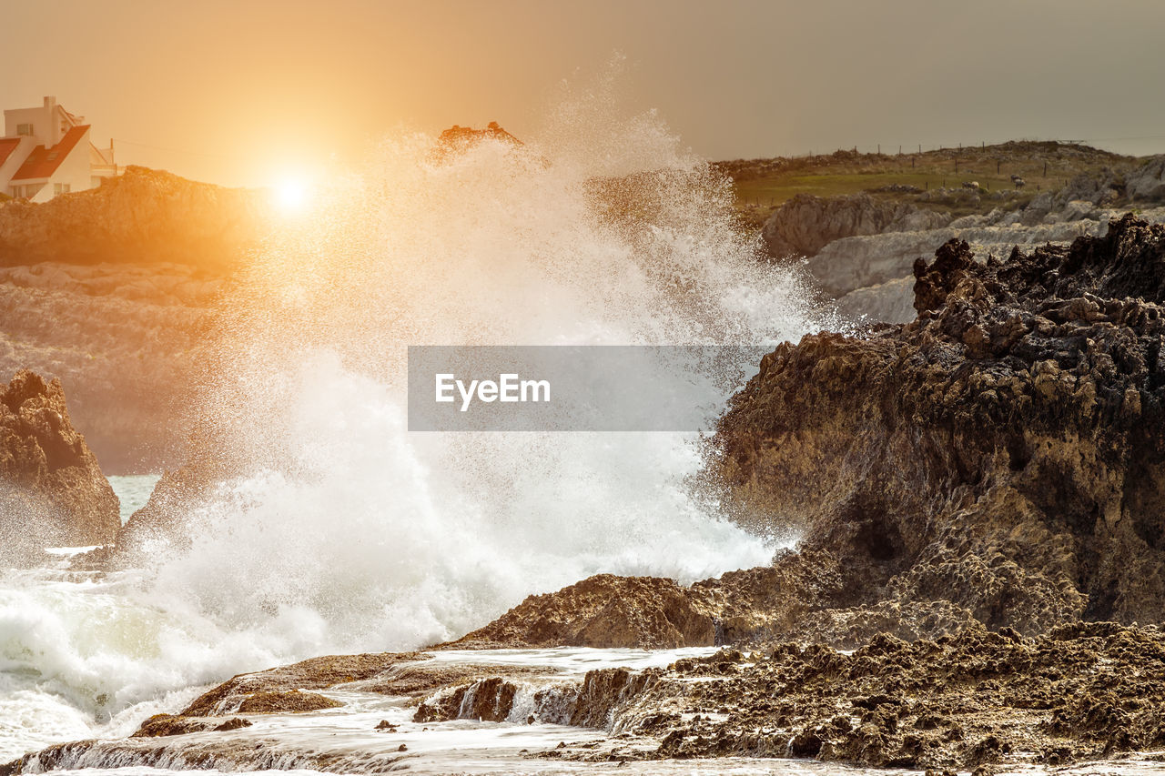 Waves crashing at sunset on the rocks of a beach in cantabria, spain. horizontal image.