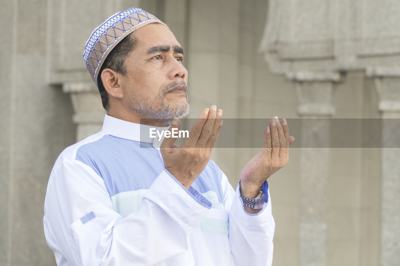 Close-up of man praying while standing at mosque