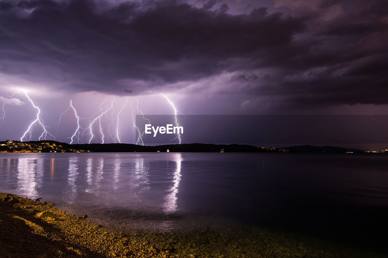 Thunderstorms in cloudy sky over lake at night