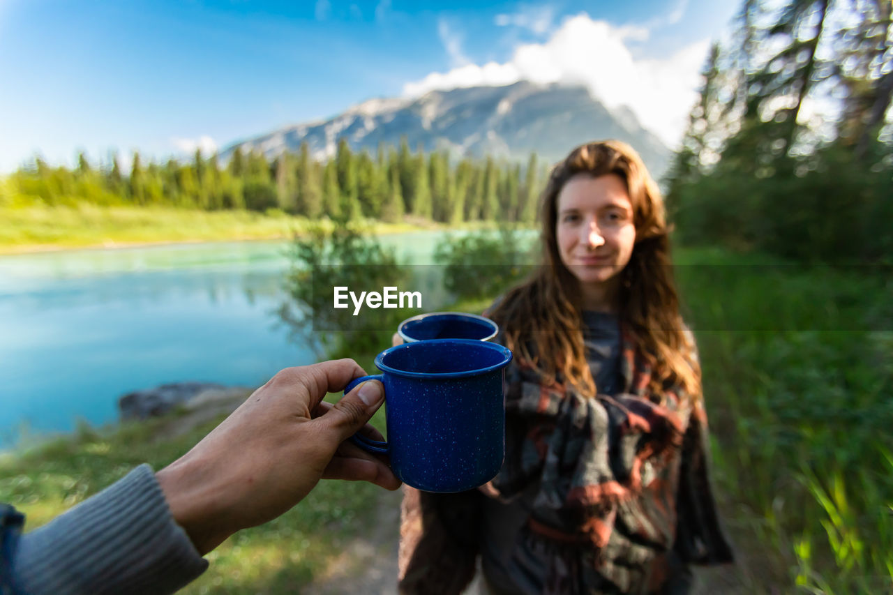 PORTRAIT OF YOUNG WOMAN DRINKING COFFEE AT MOUNTAINS