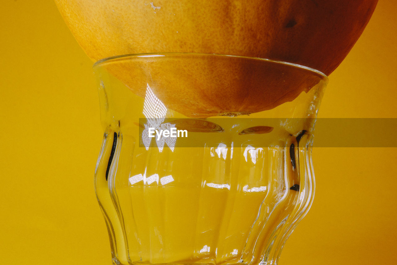 Close-up of fruit with glass against yellow background