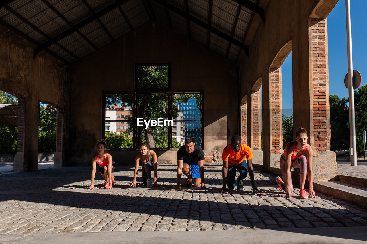 Group of diverse sportspeople standing in crouch start position ready for run during training in urban area of city