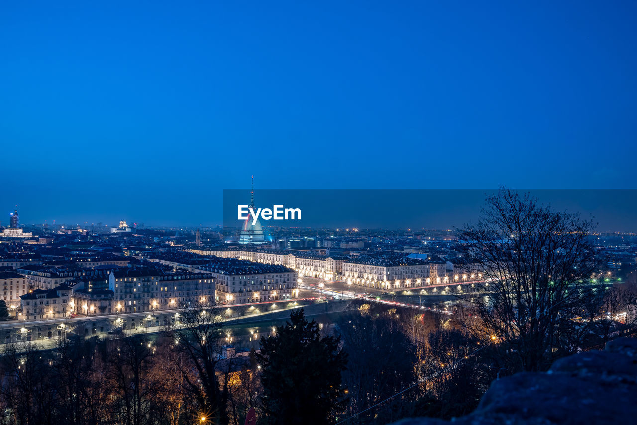 Aerial view of illuminated buildings against blue sky at night