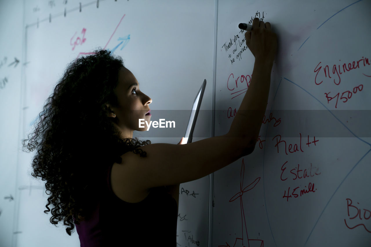 Businesswoman writing on whiteboard over tablet computer in office