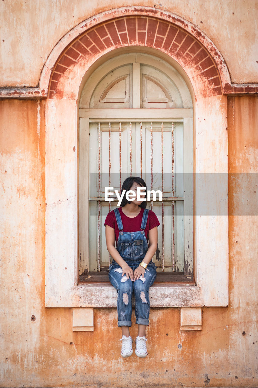 Full length of young woman sitting on window sill in old building