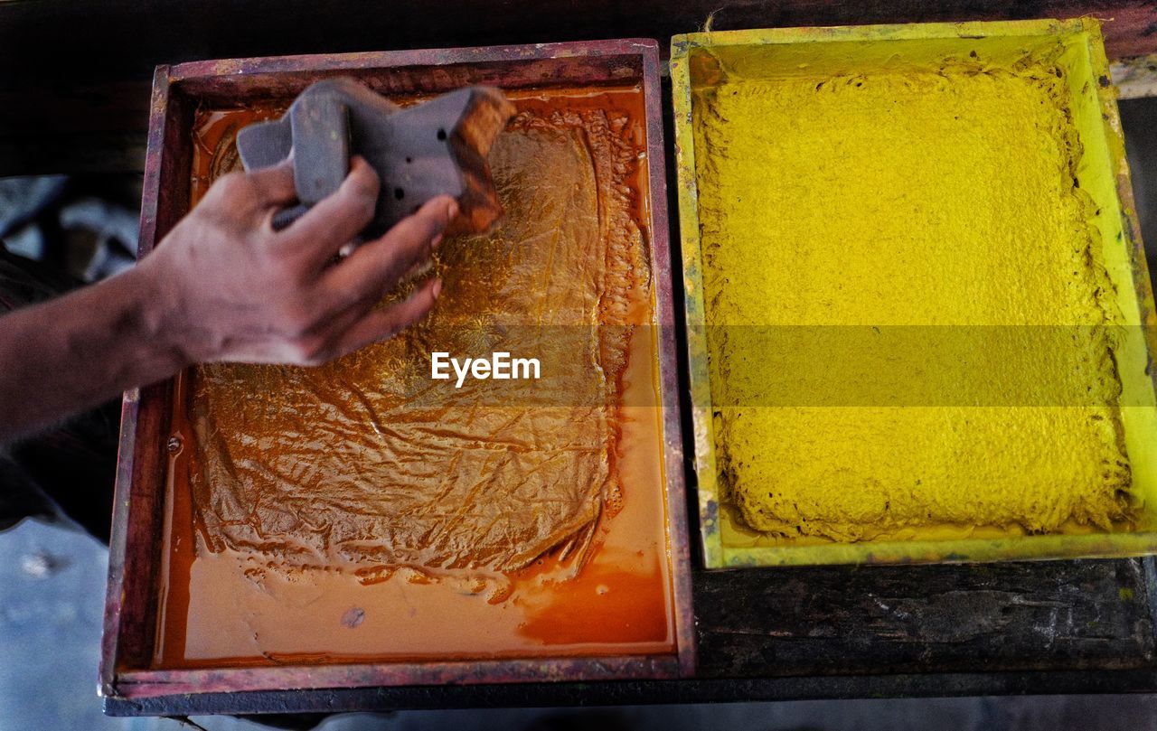 High angle view of worker holding printing block next to color container
