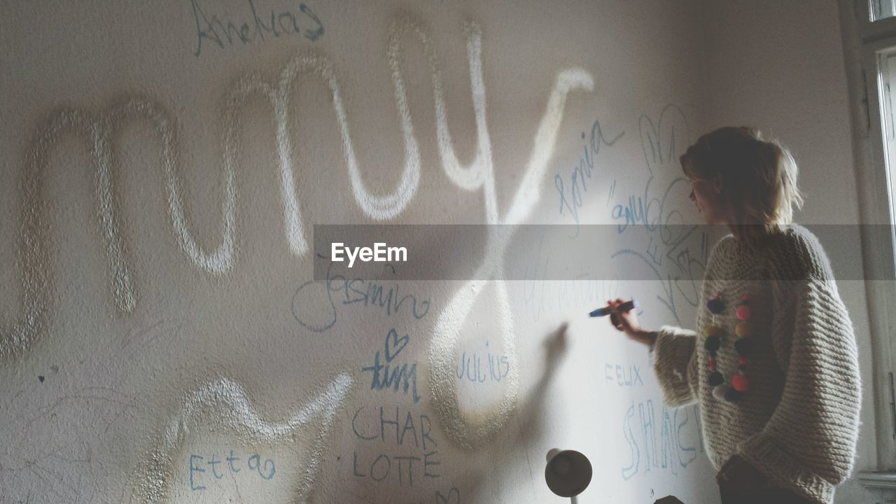 Side view of female writing on wall