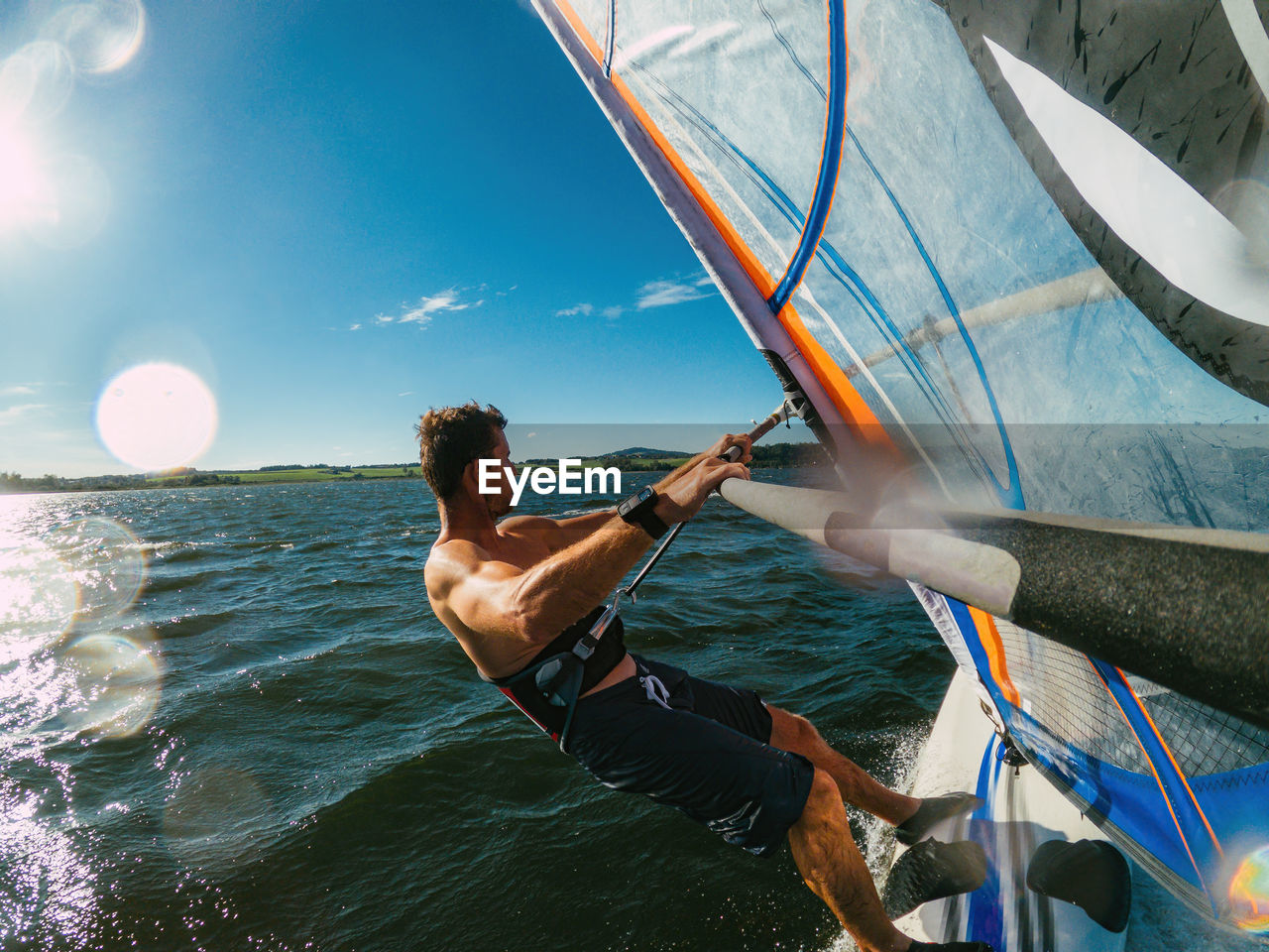 Wide-angle shot of adult man windsurfing on lake wallersee, austria