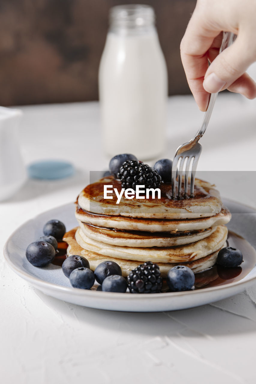 Woman sticking a fork into a stack of homemade pancakes with berries