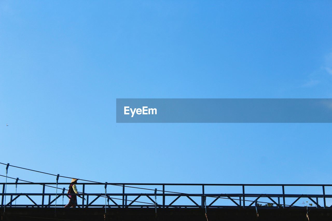 Low angle view of woman walking on bridge against clear blue sky