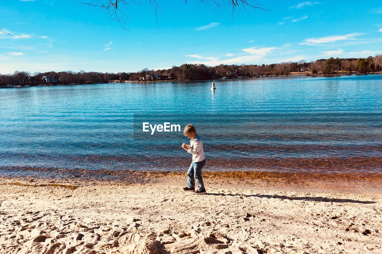 Full length of boy standing at lake against sky