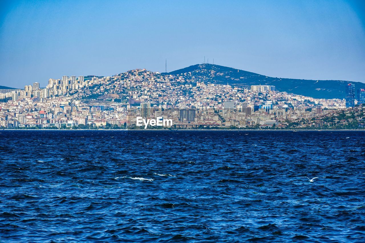 Scenic view of sea and buildings against clear blue sky