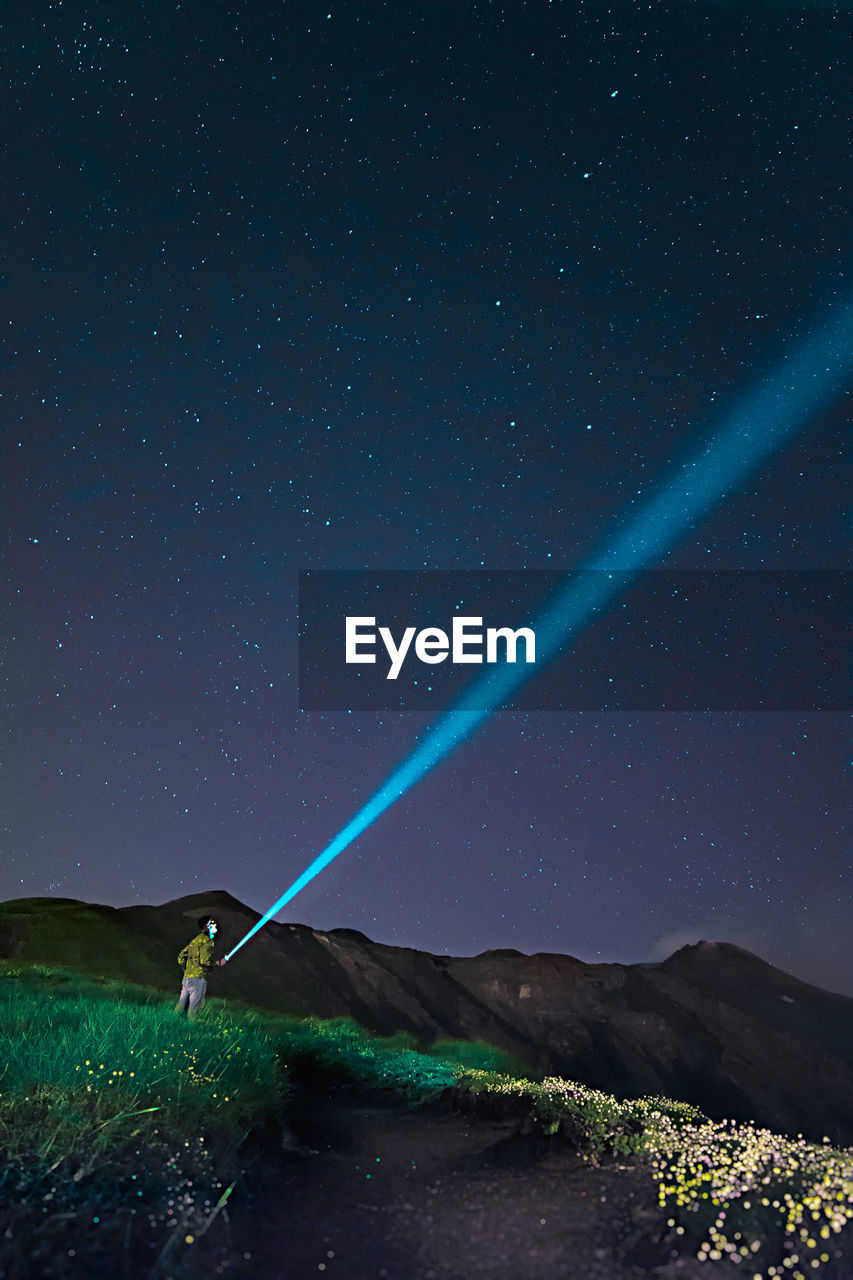 Hiker with flash light standing on field against sky