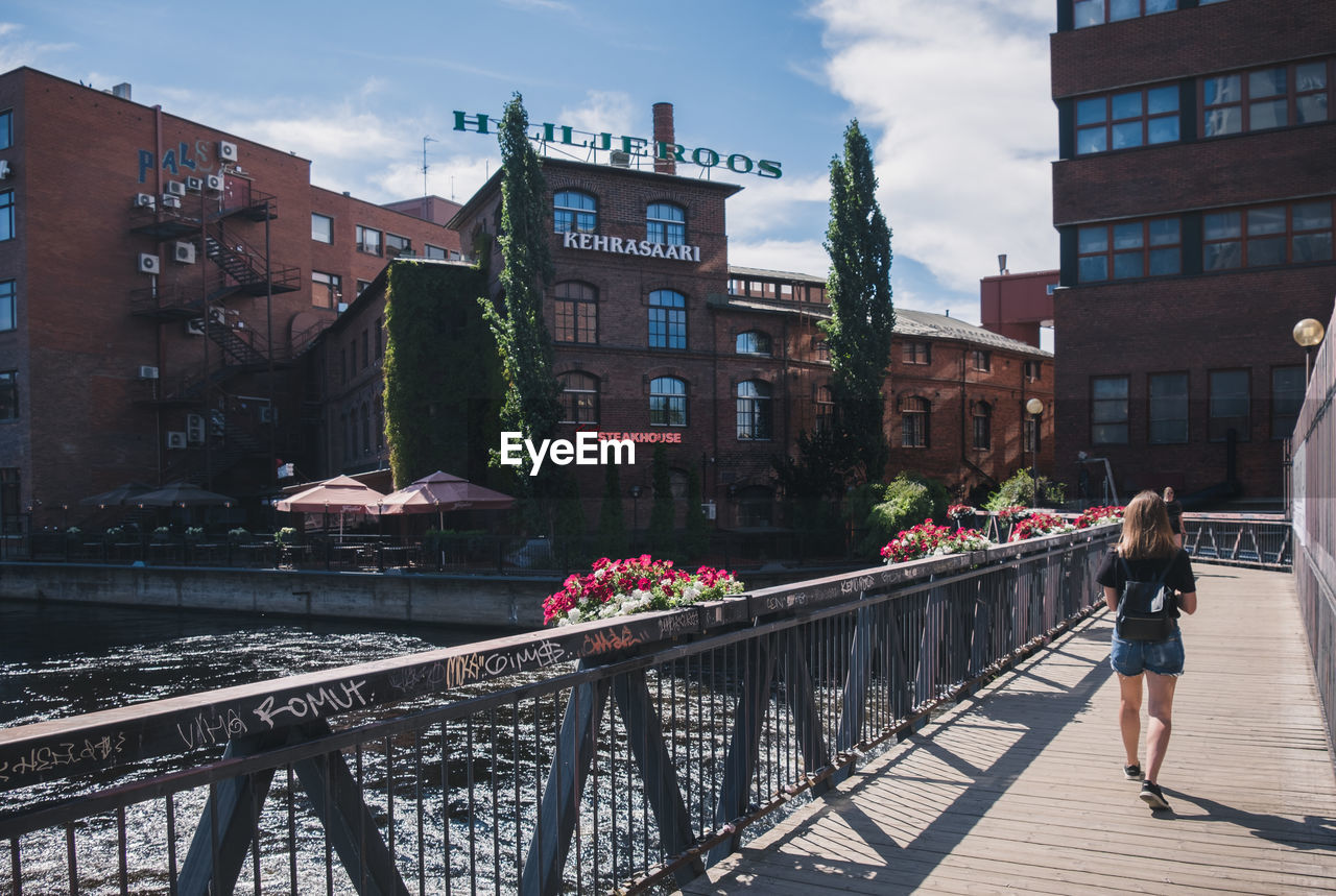 WOMAN WALKING ON CANAL BY BUILDINGS IN CITY AGAINST SKY