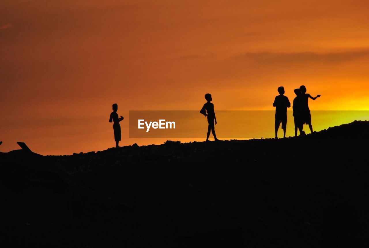 Silhouette boys on field against orange sky during sunset