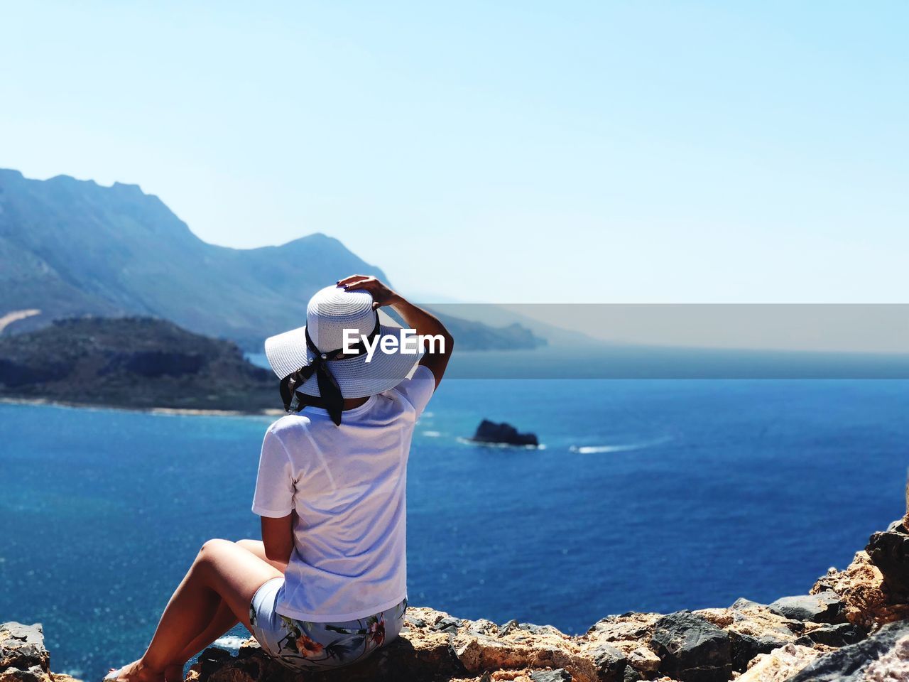 Rear view of woman sitting on shore against clear sky