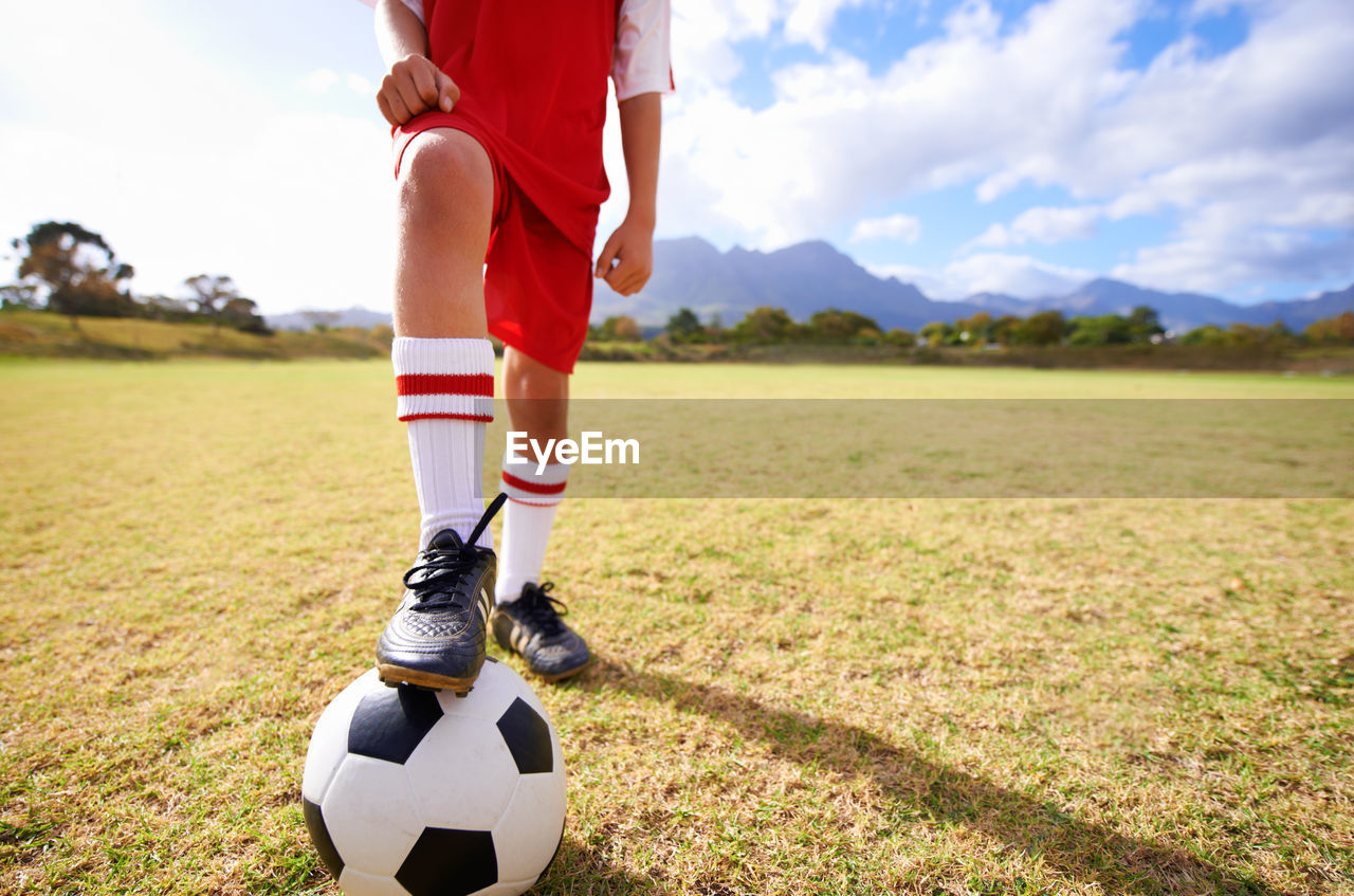 low section of man playing soccer on field against sky