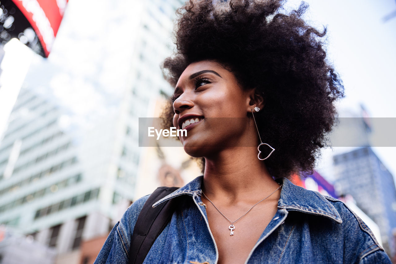 Low angle view of happy young woman with afro hairstyle in city