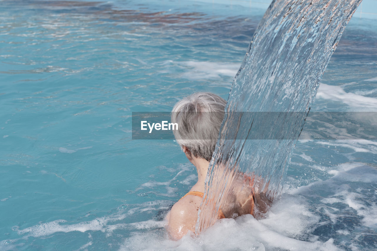 Senior woman with gray hair under flow of water falling from above. rear view.