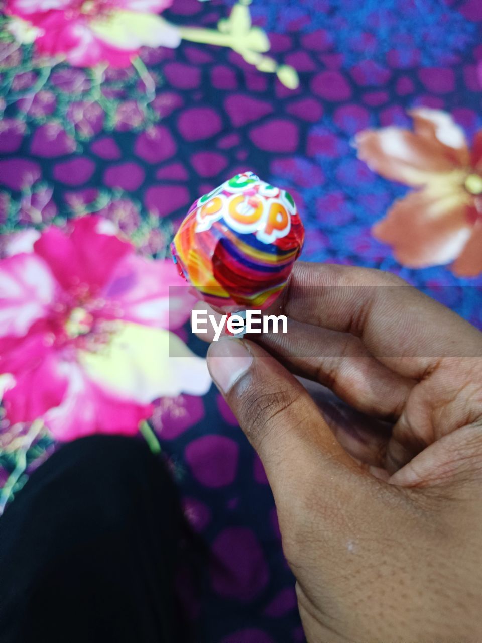 hand, holding, one person, food, flower, pink, sweet, close-up, multi colored, sweet food, freshness, flowering plant, focus on foreground, food and drink, plant, purple, finger, nature, day, personal perspective, yellow, candy, adult, dessert, outdoors, women, celebration, blue, lollipop