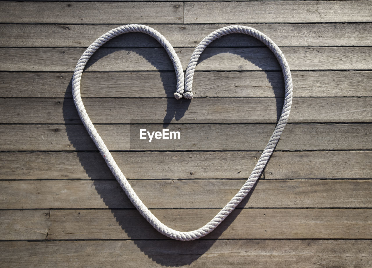 High angle view of rope arranged in heart shape over wooden plank