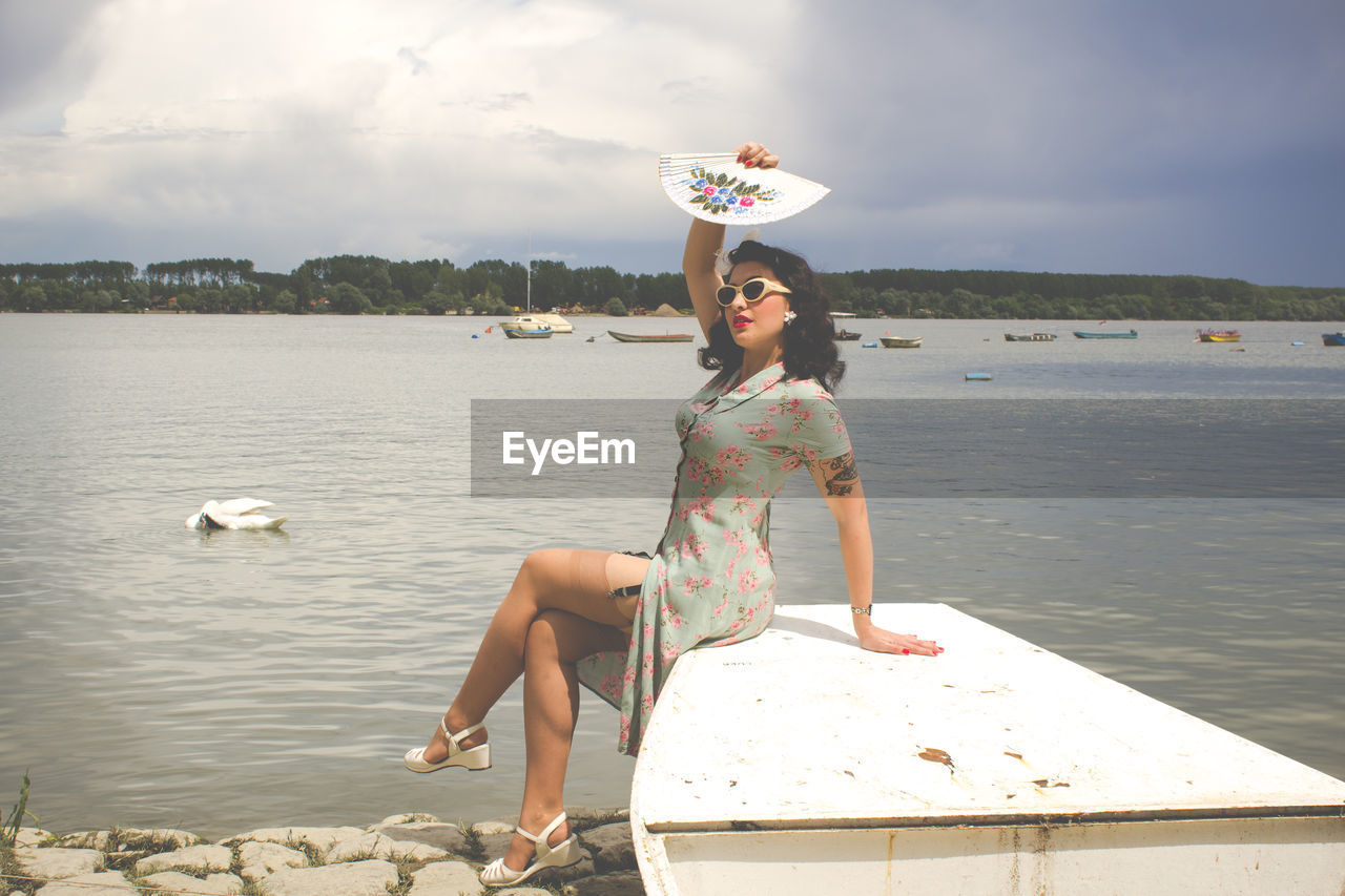 Pinup woman sitting by lake against sky