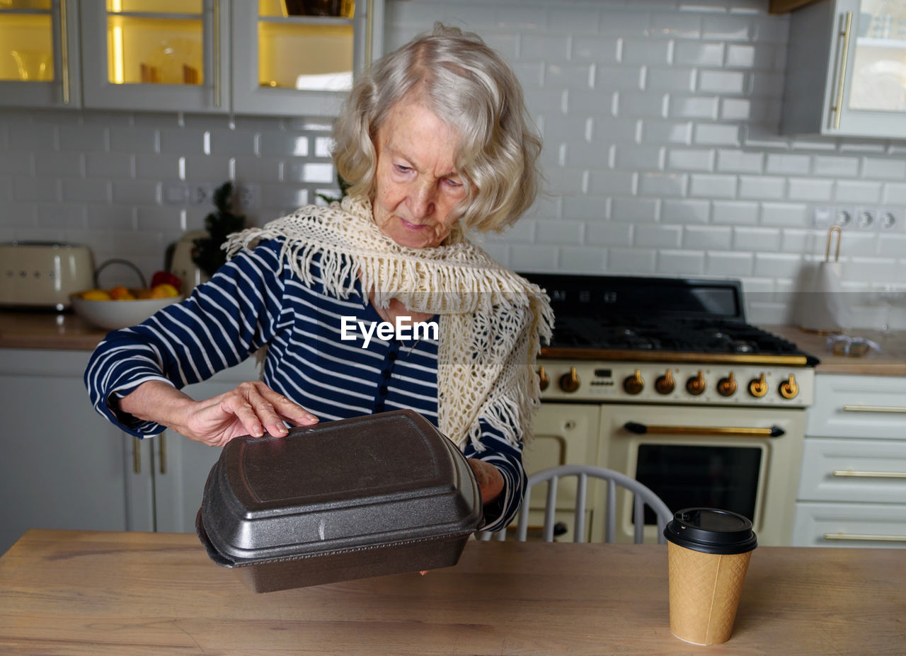 Lonely elderly woman opens food delivery from an online store