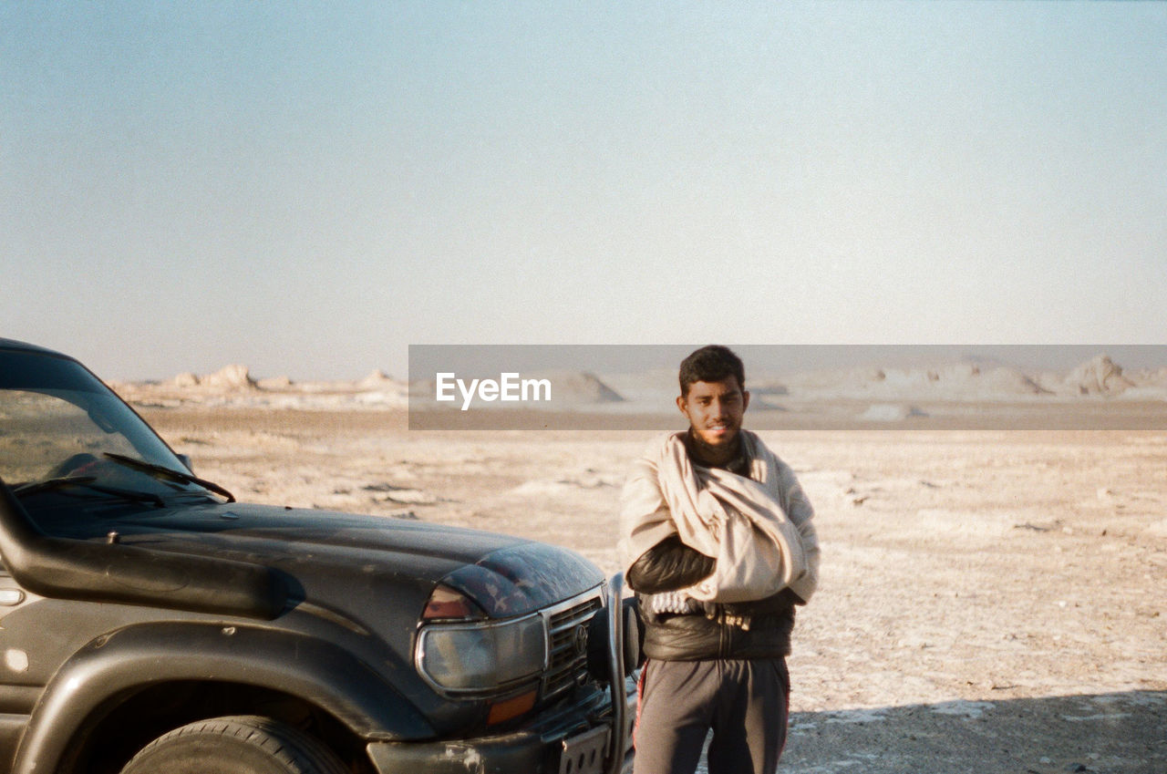 Portrait of young man standing by car on land